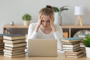 Teen with test anxiety looking at her computer with her hands on her head